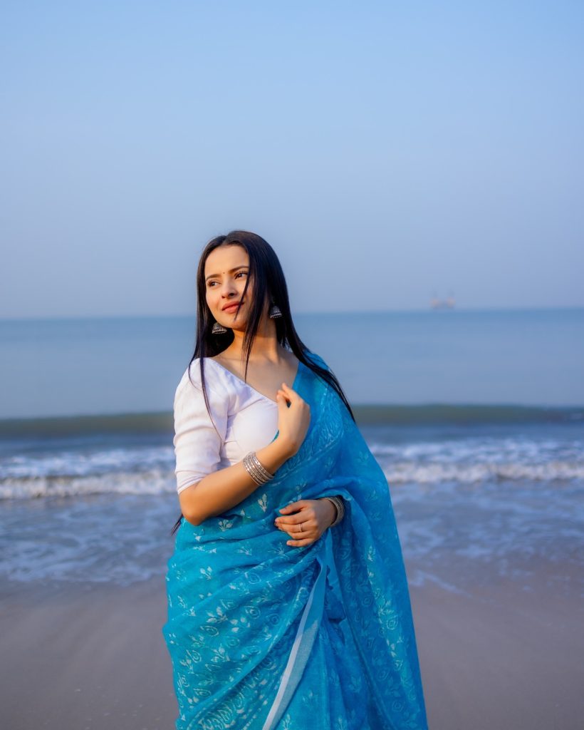 Aarushi Baruah posing in blue saree with ocean waves background