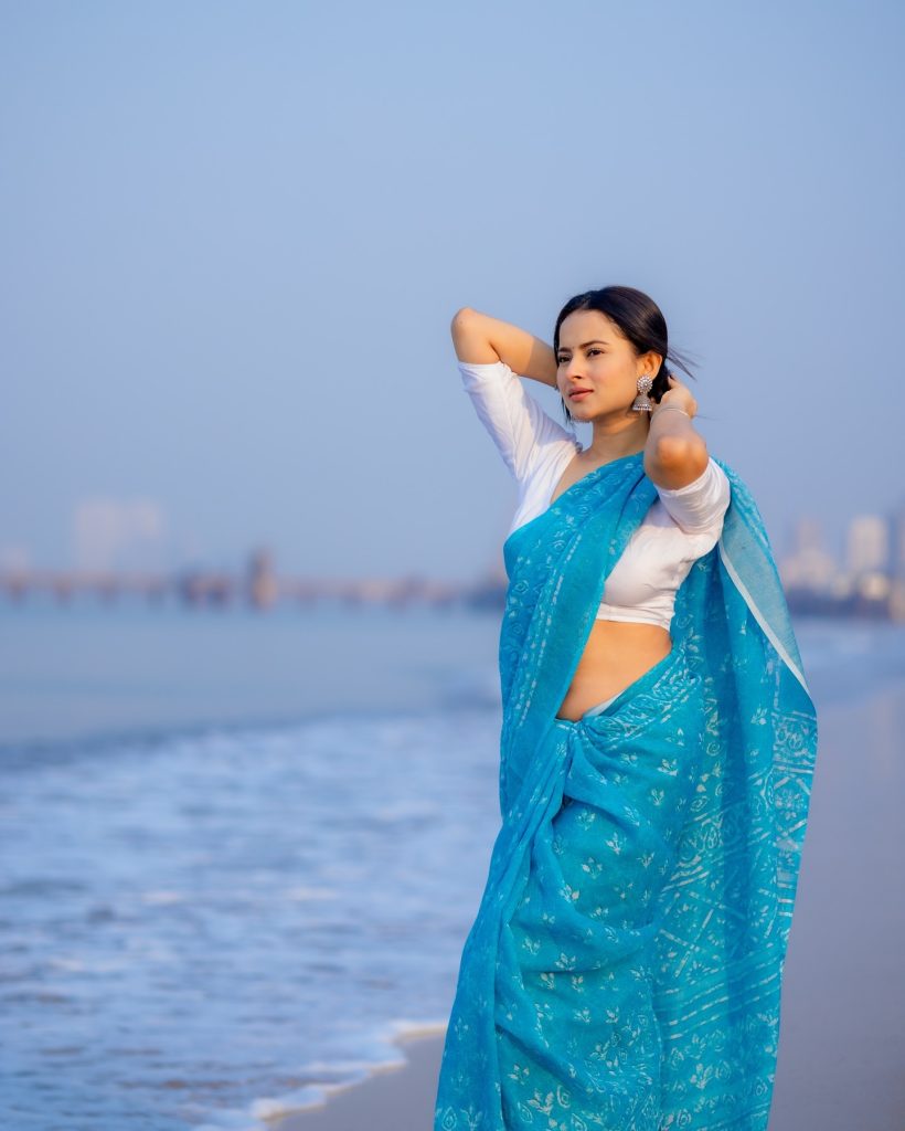 Aarushi Baruah posing in blue saree with ocean waves background