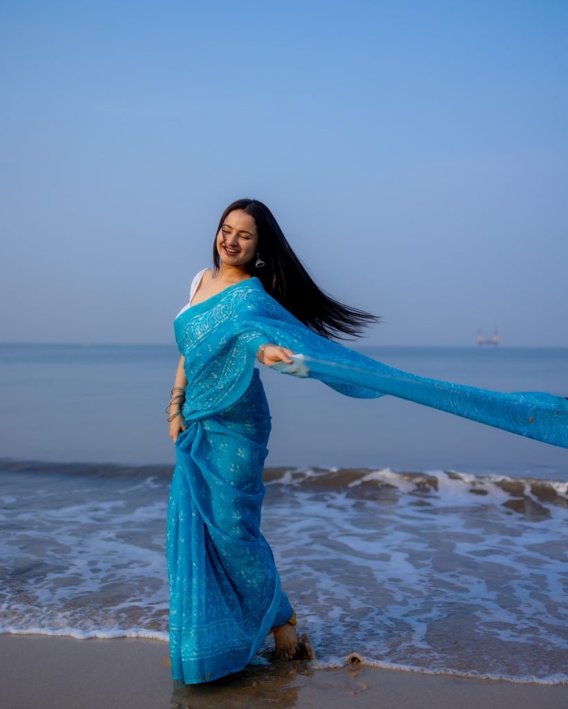 Aarushi Baruah posing in blue saree with ocean waves background