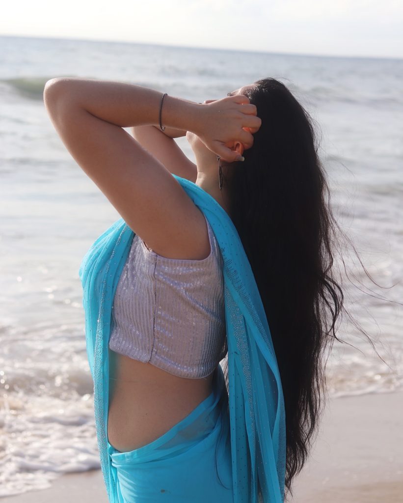 Kanduri Sudha poses gracefully with sandy shoreline and azure blue saree