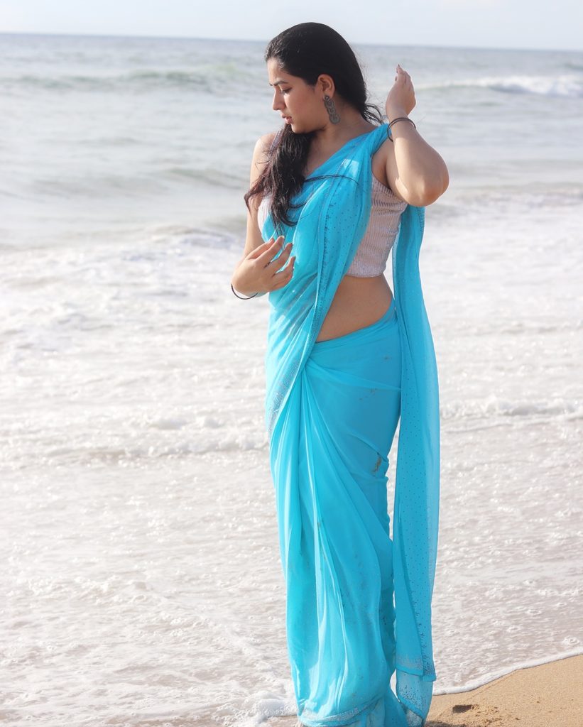 Kanduri Sudha poses gracefully with sandy shoreline and azure blue saree