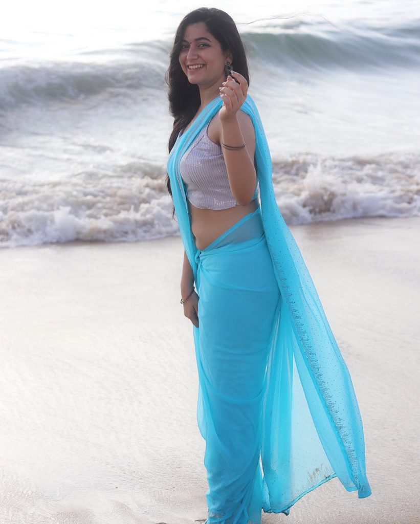 Beach waves backdrop frames Kanduri Sudha's flowing blue saree beautifully
