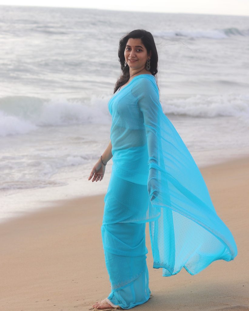 Beach waves backdrop frames Kanduri Sudha's flowing blue saree beautifully
