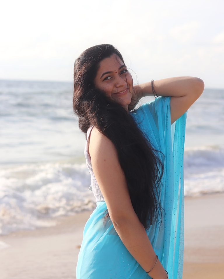 Beach waves backdrop frames Kanduri Sudha's flowing blue saree beautifully