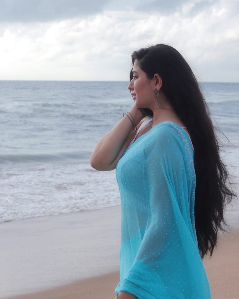 Beach waves backdrop frames Kanduri Sudha's flowing blue saree beautifully
