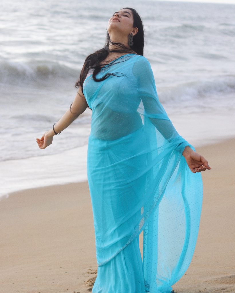 Kanduri Sudha poses gracefully with sandy shoreline and azure blue saree