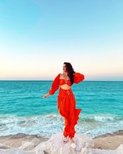 Eshanya Maheshwari twirling in orange dress on sandy beach