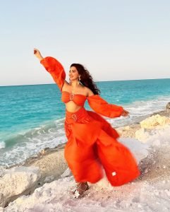 Eshanya Maheshwari playful beach pose in vibrant orange summer dress