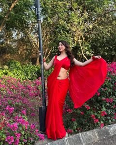 Eshanya Maheshwari in red saree standing amidst green garden foliage