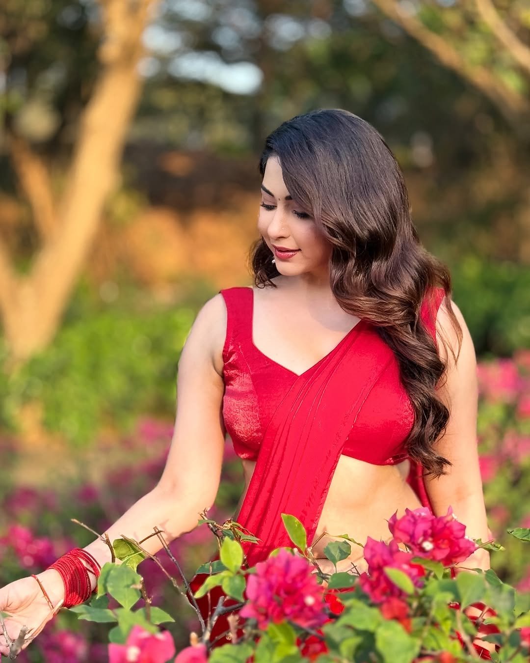 Eshanya Maheshwari in red saree standing amidst green garden foliage