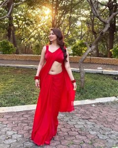 Eshanya Maheshwari in red saree standing amidst green garden foliage